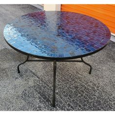 a round table with blue and purple tiles on it's top, sitting in front of an orange wall