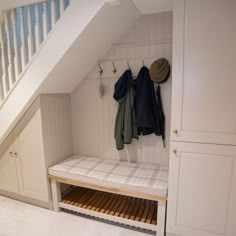 a bench with coat racks underneath the stairs in a room that has white painted walls