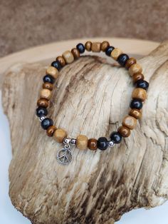 This bracelet is created with all varieties of wooden beads. It has different shades of browns with a peace sign charm hanging from it. It's earthy boho style ties together the beautiful simplicity of nature as well as the calming effects of peace. Both men and women can rock this accessory, as it is very neutral in it appearance! Cheap Bohemian Stretch Bracelet With Wooden Beads, Wooden Beads Jewelry Greatergood, Wooden Beads Jewelry, Wooden Bead Jewelry, Wooden Bead Bracelet, Wood Beads Jewelry, Bracelets Hippie, Wooden Beaded Bracelets, Hippie Accessories