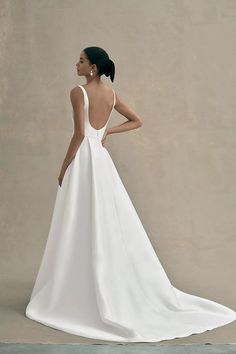 a woman in a white wedding dress with her back turned to the camera and looking off into the distance