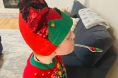 a little boy wearing a red and green hat with a spoon in it's mouth