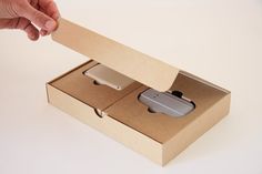 an open cardboard box with two apple products in it and someone's hand reaching for one