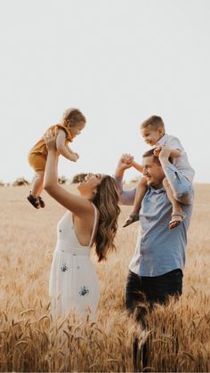 a man and woman holding two children in their hands while standing in a wheat field