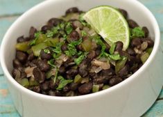 a white bowl filled with black beans and cilantro next to a lime wedge