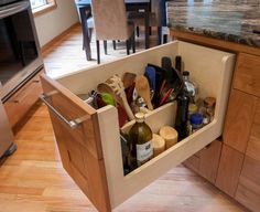 an open drawer in the middle of a kitchen with wine bottles and utensils