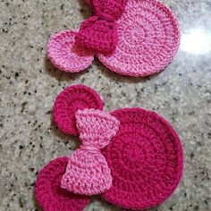 two crocheted coasters with pink bows on them sitting on a counter top