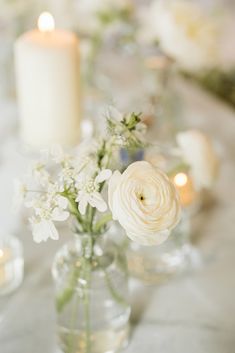 white flowers and candles are in vases on the table