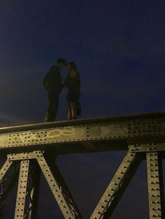 two people standing on top of a bridge at night