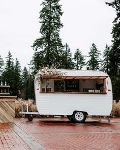 a small white trailer parked on top of a red brick road next to tall trees