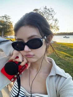 a young woman wearing sunglasses and holding a red cell phone to her ear while standing in front of a body of water