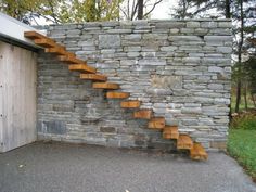 a stone wall with wooden steps leading up to the garage door in front of it