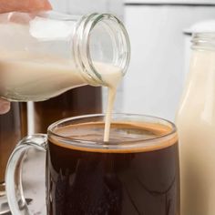 someone is pouring milk into a mug with coffee in it and another cup next to them