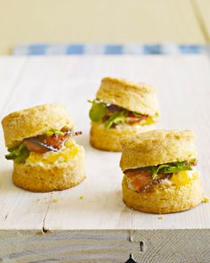 mini sandwiches with bacon and lettuce on them sitting on a wooden board, ready to be eaten