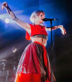 a woman in a red and black dress on stage with her arms out to the side