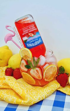 a bottle of strawberry lemonade sitting on top of a table next to sliced strawberries and lemons