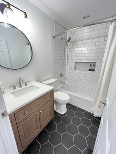 a bathroom with black and white hexagonal tile flooring, wooden cabinetry, and shower