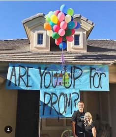 a man standing in front of a house holding a bunch of balloons with the words are you up for prom written on it