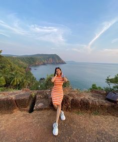 a woman in an orange and white striped dress sitting on the edge of a cliff