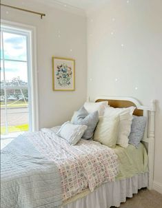 a white bed sitting next to a window with lots of pillows on top of it