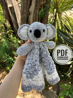 a hand holding up a crocheted koala bear in front of a tree