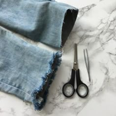 two pairs of scissors sitting on top of a pair of ripped jeans