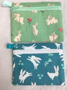 two zippered pouches with bunnies and flowers on them, one is green and the other is blue