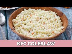 a wooden bowl filled with coleslaw on top of a blue table next to a spoon