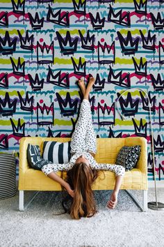 a woman laying on top of a yellow couch in front of a colorful wallpaper