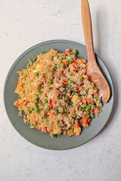 a plate with rice, peas and carrots on it next to a wooden spoon