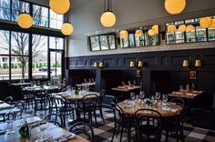 a restaurant with black walls and checkered flooring, large windows, yellow lamps hanging from the ceiling