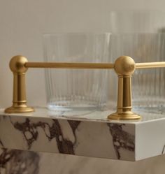 two glasses are sitting on a marble shelf with brass fittings and one is empty