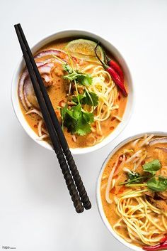 two bowls filled with noodles and vegetables next to chopsticks on a white surface