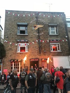 a group of people standing in front of a brick building with flags on the side