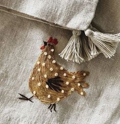 a small brown chicken sitting on top of a bed next to a tasseled pillow