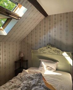 a bed sitting under a window in a bedroom next to a wall papered ceiling