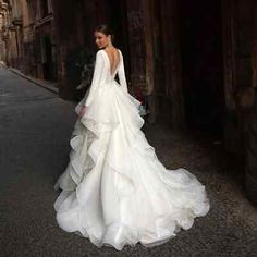 a woman in a wedding dress is walking down the street with her back to the camera