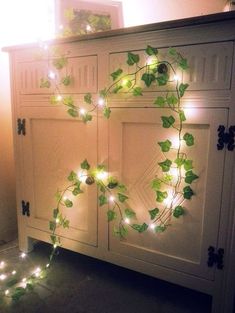 a white cabinet with green ivy vines on it and lights strung from the doors behind it