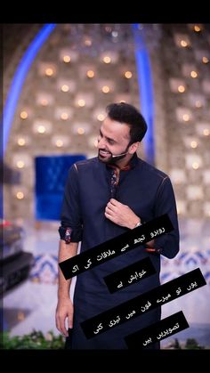 a man standing in front of a tv screen wearing a black shirt and tie with arabic writing on it