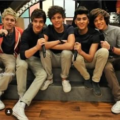 four young men sitting on a couch posing for the camera with their arms around each other