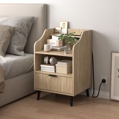 a nightstand with books and plants on it next to a bed