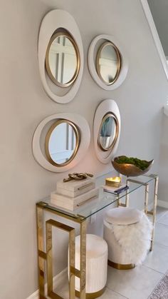 three round mirrors on the wall above a glass table with two stools and a white ottoman