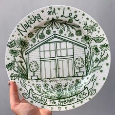 a hand holding a green and white plate with a drawing of a house on it