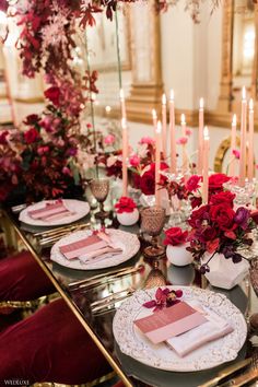 the table is set with pink and red flowers, candles, and napkins on it