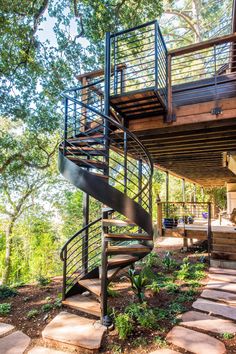 a spiral staircase leading up to the upper level of a house with stone steps and trees in the background