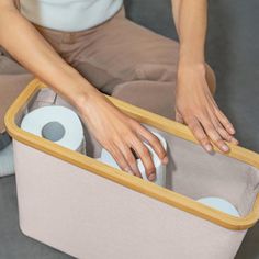 a woman sitting on the floor with her hands in a storage bin that is holding toilet paper