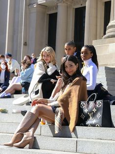 several young women sitting on the steps in front of a building with their legs crossed