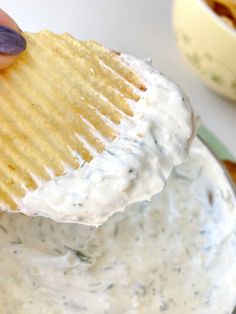 a hand holding a cracker over a bowl of dip