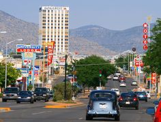 cars are driving down the street in front of tall buildings and mountain range behind them