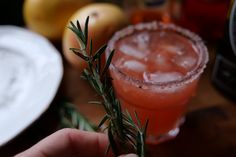 a person holding up a rosemary sprig next to a drink