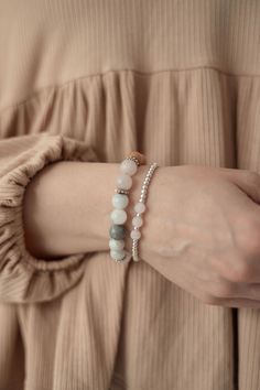 a woman's arm with two bracelets on it, one is wearing a beige top and the other has a white bea